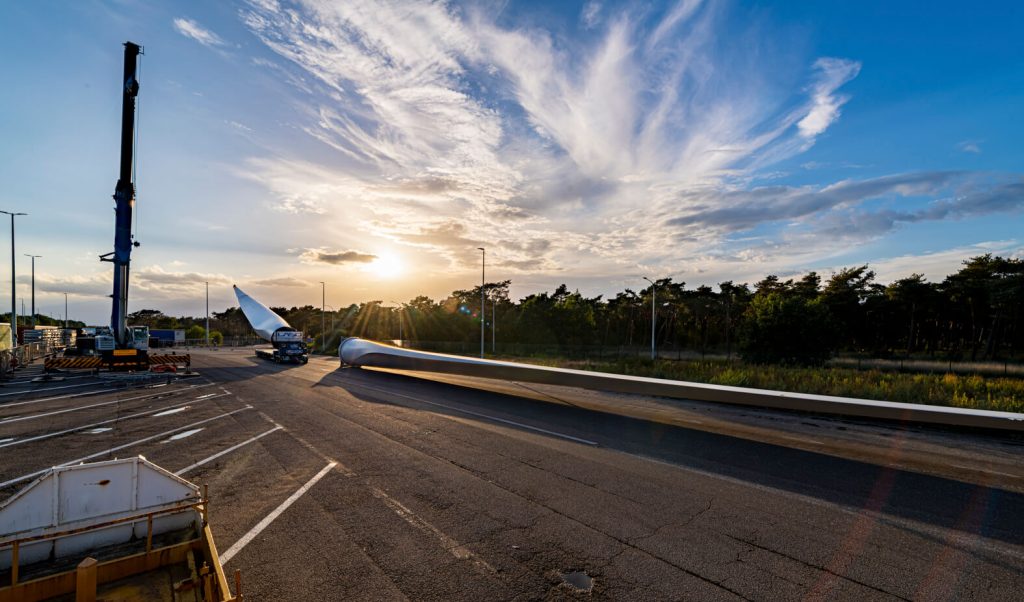 Windmolenblad op vrachtwagen bij zonsondergang.