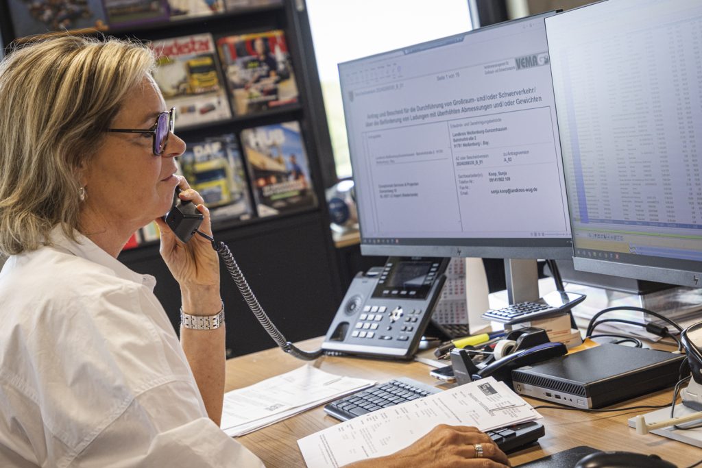 Vrouw aan de telefoon bij computerschermen op kantoor.