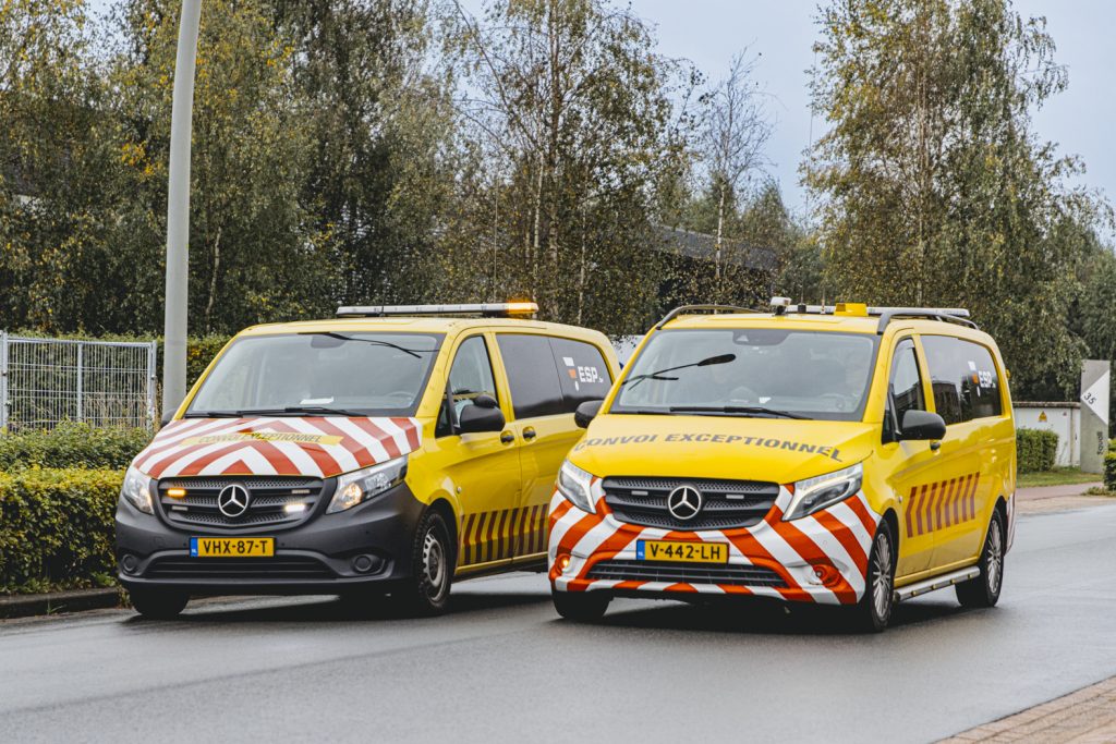 Twee gele escortewagens op een regenachtige weg.