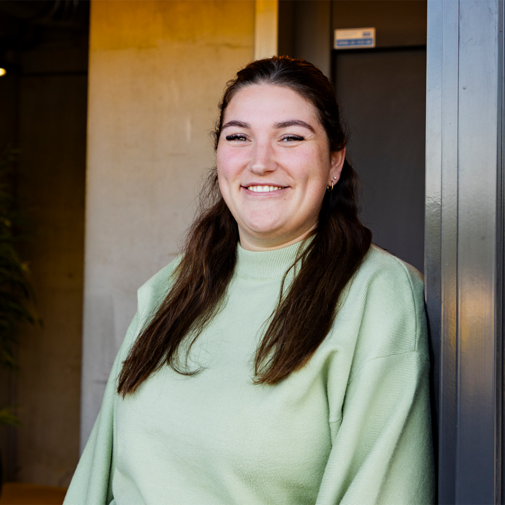 Vrouw glimlacht naast muur in gebouw.